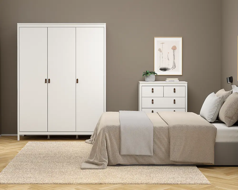 Et moderne soveværelse med neutrale farver, der har en stor seng med beige sengetøj og flere puder, et hvidt garderobeskab med tre døre og enkle greb samt en matchende hvid kommode med sorte greb. Rummet har også et lyst beige tæppe på trægulv, et indrammet minimalistisk kunsttryk over kommoden og en lille potteplante som dekoration. Stilen er enkel og minimalistisk.