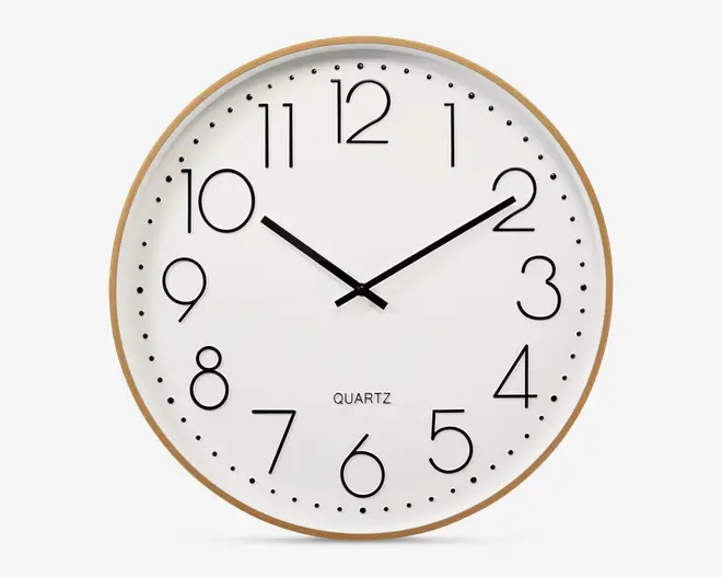Rund vægur med en lys træramme og hvid urskive. Uret har store, sorte arabertal og sorte time- og minutvisere. Der er ingen sekundviser. Designet er minimalistisk med jævnt fordelte sorte prikker for hvert minut. Ordet 'QUARTZ' står trykt over klokken 6.