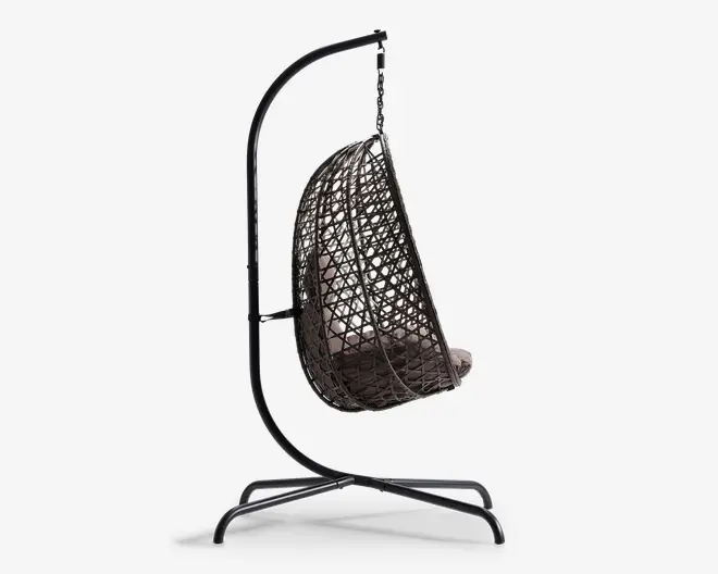 Sidevisning af en hængende æggestol med mørk metalramme og flettet rattan-lignende sæde. Stolen er ophængt i et buet stativ og har en tyk, lysefarvet hynde for ekstra komfort. Sædets åbne gitterdesign giver god luftcirkulation og et moderne udseende.