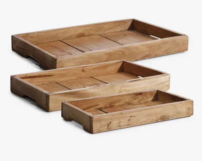 Sæt med tre rektangulære bakker lavet af naturtræ, hver med et rustikt, ubehandlet udseende. Bakkerne har tykke, solide sider og synlige træårer samt bund af sammensatte træplanker for ekstra struktur. Hver bakke har forskellig størrelse, så de kan stables eller lægges ind i hinanden. Kanterne er let forhøjede for at holde indholdet på plads, og der er udskårne håndtag i de korte sider for nem bæring.