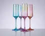 Sæt med fire høje, riflede glas i forskellige gennemsigtige farver: blå, lyse lilla, pink og rav. Hvert glas har lodrette rillede detaljer på skålen, slanke stilke og en blank overflade. Glassene står oprejst på en reflekterende overflade, hvilket fremhæver deres elegante og moderne design.