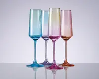 Sæt med fire høje, riflede glas i forskellige gennemsigtige farver: blå, lyse lilla, pink og rav. Hvert glas har lodrette rillede detaljer på skålen, slanke stilke og en blank overflade. Glassene står oprejst på en reflekterende overflade, hvilket fremhæver deres elegante og moderne design.