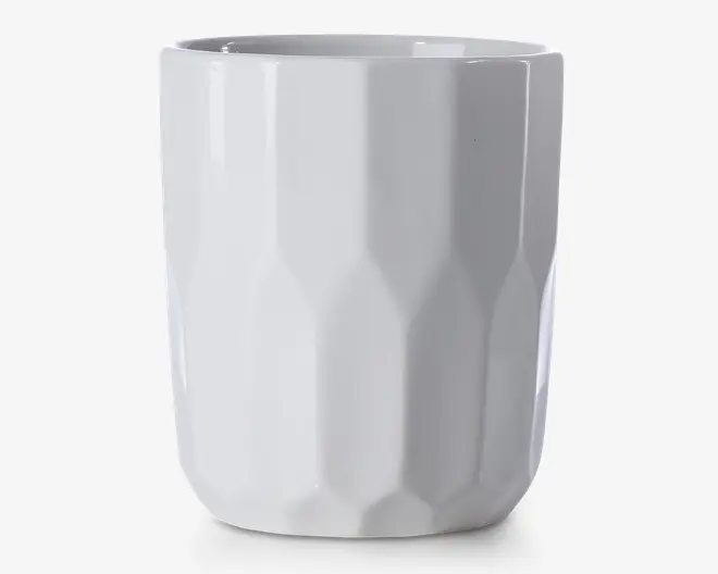 En høj, hvid keramikkop med blank overflade og et facetteret, geometrisk mønster. Koppen har en lige, cylindrisk form uden hank, hvilket giver et moderne og minimalistisk udtryk.