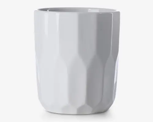 En høj, hvid keramikkop med blank overflade og et facetteret, geometrisk mønster. Koppen har en lige, cylindrisk form uden hank, hvilket giver et moderne og minimalistisk udtryk.