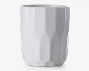 En høj, hvid keramikkop med blank overflade og et facetteret, geometrisk mønster. Koppen har en lige, cylindrisk form uden hank, hvilket giver et moderne og minimalistisk udtryk.