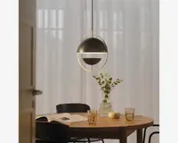 En moderne pendellampe med kugleformet design, mat sort finish og en tynd gylden ring omkring midten. Lyset udsendes fra en vandret åbning, der deler kuglen, hvilket giver et blødt og behageligt lys. Lampen hænger fra en slank sort ledning og tilfører rummet et minimalistisk udtryk.