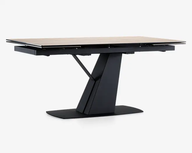 Rektangulært bord med en lys, glat bordplade og et moderne, geometrisk sort søjleben. Basen har et vinklet, skulpturelt design med en bred, flad bund for stabilitet. Bordet ser ud til at have en udtræksfunktion, hvilket ses på de synlige samlinger og beslag under bordpladen.