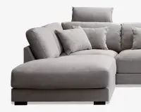 Sektionssofa med chaiselong på venstre side, betrukket med lysegråt tekstureret stof. Sofaen har tykke, bløde sæde- og ryghynder for ekstra komfort samt flere matchende pyntepuder. Designet er moderne og kantet med rene linjer og en høj nakkestøtte på én sektion for ekstra støtte.
