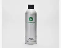 En høj, cylindrisk sølvfarvet flaske med sort skruelåg. Etiket med grønt 'G'-logo og mærket 'Guardian Furniture Care'. Produktet er angivet som trærenser, med yderligere tekst på flere sprog nederst. Flasken har et slankt, moderne design og ser ud til at være lavet af metal.