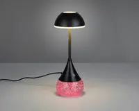 Moderne bordlampe med sort, kuppelformet skærm og en slank, central stang. Basen er konisk og har en touch-følsom tænd/sluk-knap. Den nederste del af basen er fyldt med lyserødt glimmer, som er oplyst indefra og skaber en glitrende effekt. Lampen får strøm via en synlig sort ledning.