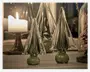 Sæt af dekorative glasskulpturer formet som stiliserede træer, lavet af klart glas med et diskret grønt skær. Hver figur har en glat, rund fod og lange, spidse grene, hvilket giver et moderne og elegant udtryk. Glasset er blankpoleret og reflekterer lyset flot. Produkterne er udstillet på en overflade med et tændt stearinlys i baggrunden, hvilket skaber en varm og hyggelig stemning.