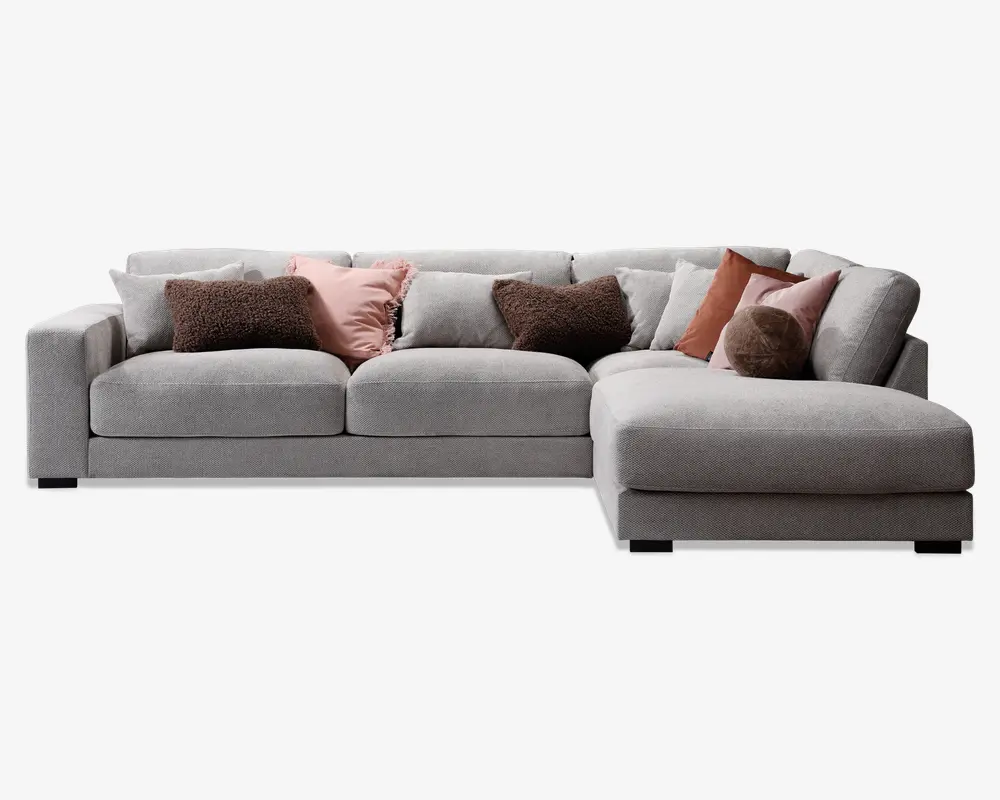 Moderne hjørnesofa med chaiselong til højre, betrukket med lysegråt stof. Sofaen har brede, firkantede armlæn og dybe, bløde sædehynder for ekstra komfort. Leveres med flere pyntepuder i forskellige teksturer og farver, herunder brun, rosa og rust, som giver et hyggeligt og stilfuldt udtryk.