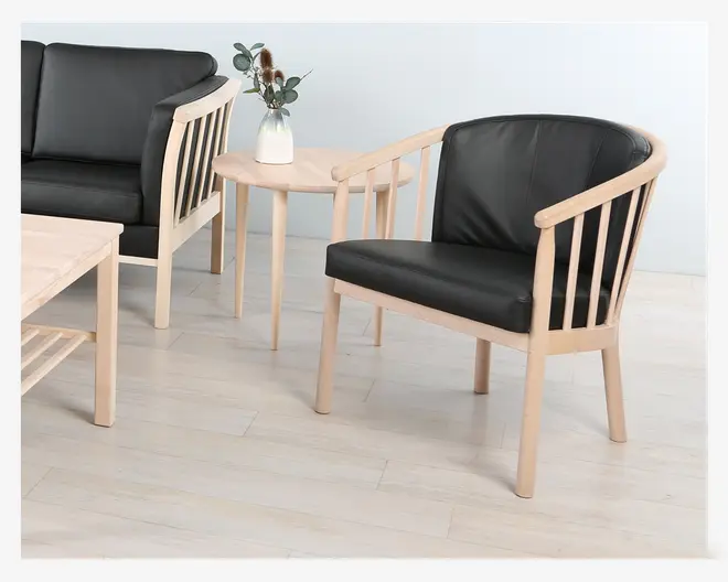 Lænestol med stel i lyst træ og sorte polstrede sæde- og ryghynder. Stolen har afrundede armlæn og lodrette tremmer på ryglænet. Sæde- og rygpuderne er betrukket med glat sort materiale, hvilket giver et moderne og minimalistisk udtryk. Benene er lige og let tilspidsede, i samme lyse træfinish.