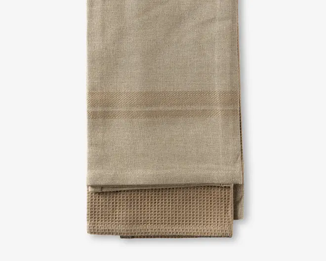 Sæt med to beige viskestykker, det ene med en glat, tæt vævet struktur og det andet med et vaffelmønster. Begge viskestykker har en neutral, ensfarvet tone og ser ud til at være lavet af absorberende bomuldsmateriale, velegnet til at tørre service eller hænder.