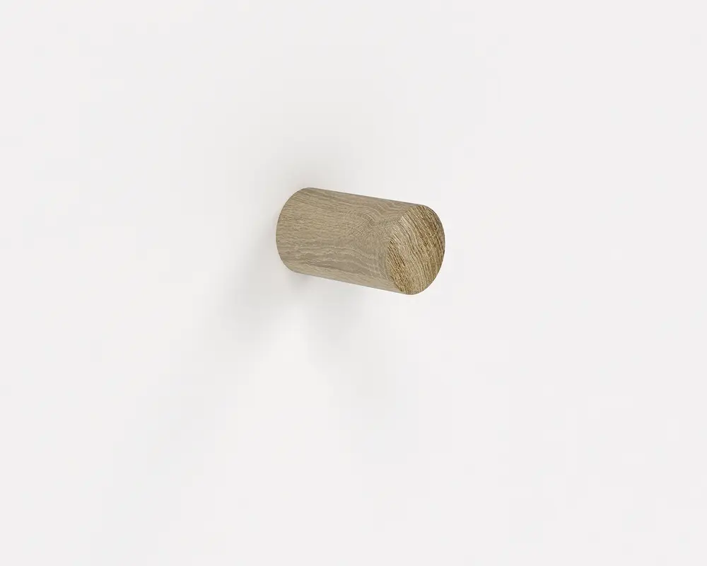 Et cylindrisk træknop med en naturlig lys egetræsfinish, monteret vandret på en hvid væg. Træets årer er synlige, hvilket giver et enkelt og minimalistisk udtryk.