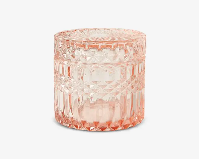 Rund beholder lavet af lyserødt glas med tilhørende låg. Overfladen har et indviklet diamant- og geometrisk mønster, som giver et vintage og dekorativt udtryk. Glasset er tykt og reflekterende, og låget passer tæt på toppen.