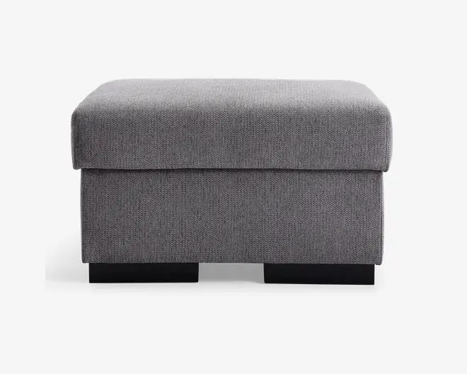 Rektangulær puf med blød, polstret top og betrukket med et tekstureret lysegråt stof. Designet er enkelt og moderne med rene linjer og en firkantet form. Puffen står på lave, solide sorte ben, og stoffet er stramt monteret for et pænt udseende.