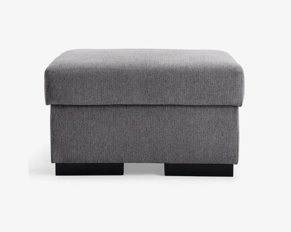 Rektangulær puf med blød, polstret top og betrukket med et tekstureret lysegråt stof. Designet er enkelt og moderne med rene linjer og en firkantet form. Puffen står på lave, solide sorte ben, og stoffet er stramt monteret for et pænt udseende.