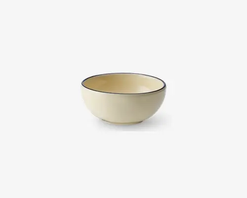 En rund, cremefarvet skål med en glat, blank overflade. Skålen har en diskret, mørk kant langs øverste kant, hvilket giver et elegant modspil til det enkle design. Både inderside og yderside har samme farve, og skålen har en blødt buet form med en stabil bund.