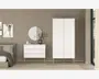 Et moderne, minimalistisk soveværelsesmiljø med en hvid kommode, der har tre store skuffer og to mindre øverste skuffer, alle med små runde greb. Kommoden står på skråtstillede ben i lyst træ. Ved siden af står et matchende hvidt garderobeskab med to låger og to nederste skuffer, også med små runde greb og ben i lyst træ. Møblerne har et rent, enkelt design med glatte overflader og diskrete detaljer. Over kommoden er der monteret et rundt spejl, og på toppen står en dekorativ vase med grene. Det samlede udtryk er stilrent og moderne med neutrale farver og naturlige træelementer.