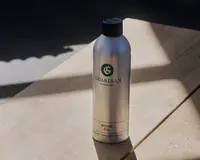 En høj, cylindrisk sølvfarvet metalflaske med sort skruelåg. Etiketten har teksten 'Guardian Furniture Care' og 'Wood Oil' i grøn og sort skrift. Flasken har et minimalistisk design med tydelig og letlæselig mærkning og virker robust og nem at håndtere. Velegnet til opbevaring og dosering af træolie til møbelpleje.