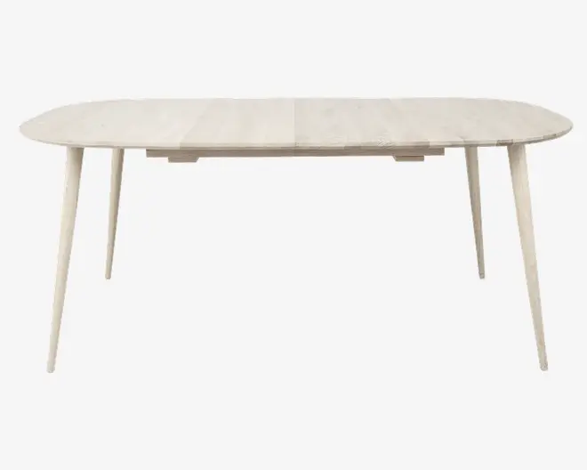 Et lyst, ovalt bord i træ med glatte, afrundede kanter. Bordpladen har et diskret træmønster og understøttes af fire slanke, let udadskrånende ben, hvilket giver et moderne og minimalistisk udtryk.