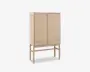 Høj skab lavet af lyst træ med to låger, der har vandrette lameldetaljer. Skabet står på fire slanke ben, som er forbundet med støttebøjler, hvilket giver et løftet og let udtryk. Designet er minimalistisk og moderne med rene linjer og en naturlig træfinish.