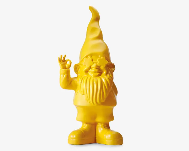 Dekorativ figur i klar gul farve med et finurligt nissedesign, der har en høj, spids hue, langt struktureret skæg og store støvler. Nissen smiler og laver et 'OK'-håndtegn med højre hånd. Overfladen er glat og blank, hvilket giver et moderne og legende udtryk.