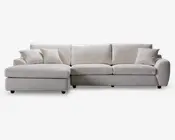 En stor, moderne hjørnesofa betrukket med lysebeige stof. Sofaen har en venstrevendt chaiselong, brede armlæn og bløde sæde- og ryghynder for ekstra komfort. Der medfølger fire matchende pyntepuder, som giver ekstra hygge og stil. Designet er enkelt og moderne, velegnet til rummelige stuer.