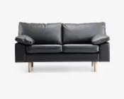 En moderne to-personers sofa betrukket med glat sort læder og udstyret med bløde, aftagelige ryg- og sædehynder. Sofaen har brede, polstrede armlæn og står på fire lyse træben, hvilket giver et nutidigt udtryk. Designet er minimalistisk, og materialerne tyder på nem vedligeholdelse og god komfort.