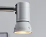 En hvid, cylindrisk og kegleformet justerbar lampe monteret på en vandret kromstang, med et varmt lys, der skinner nedad fra undersiden.