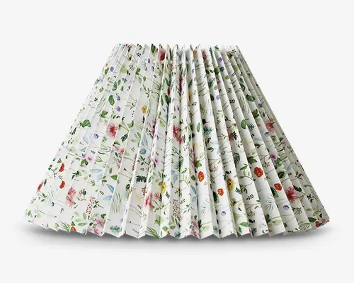 Plisseret lampeskærm med hvid baggrund og et fint, flerfarvet blomstermønster. Designet har forskellige små blomster og grønne blade i nuancer af rød, lilla, blå og gul, hvilket giver et frisk og livligt udtryk. Plisseringen giver en tekstureret, struktureret overflade, og formen er bred forneden og smal foroven.