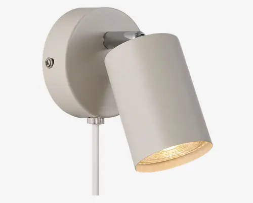 Væghængt spotlampe med cylindrisk, mat hvid metalskærm. Lampens hoved kan justeres, så lyset kan rettes efter behov. Armaturet har en rund base med en synlig skrue og en ledning, der går ud fra bunden. Indersiden af skærmen er reflekterende for at forstærke lysudbyttet.