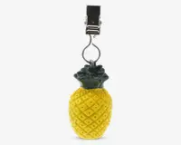 Et dekorativt element formet som en ananas med en gul, mønstret overflade og grønne blade i toppen. Den er fastgjort til en sølvfarvet metalclips, hvilket gør den velegnet til ophængning eller fastgørelse på andre genstande.