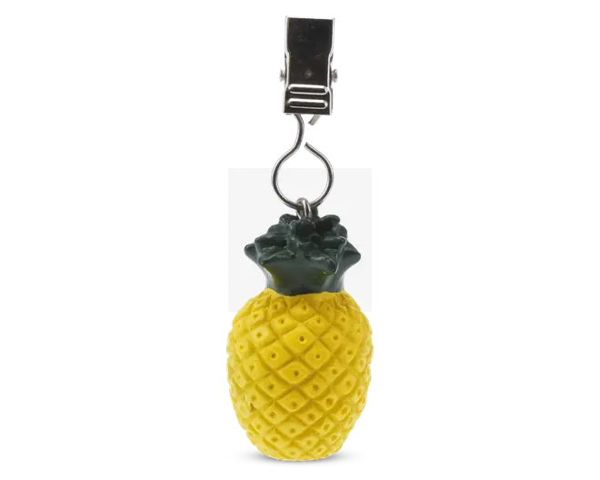 Et dekorativt element formet som en ananas med en gul, mønstret overflade og grønne blade i toppen. Den er fastgjort til en sølvfarvet metalclips, hvilket gør den velegnet til ophængning eller fastgørelse på andre genstande.