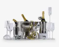 Et festligt arrangement med to flasker champagne i sølvfarvede isspande, omgivet af forskellige typer glas såsom vinglas, champagneglas og tumblere. Opsætningen inkluderer også en cocktailshaker, metalliske guldfarvede bånd og flere små sølvfarvede diskokugle-dekorationer, hvilket skaber en elegant og festlig stemning.
