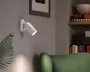 Hvid vægmonteret spotlampe med justerbart cylindrisk lampehoved på en rund bagplade, vinklet nedad og med en fokuseret lysstråle.