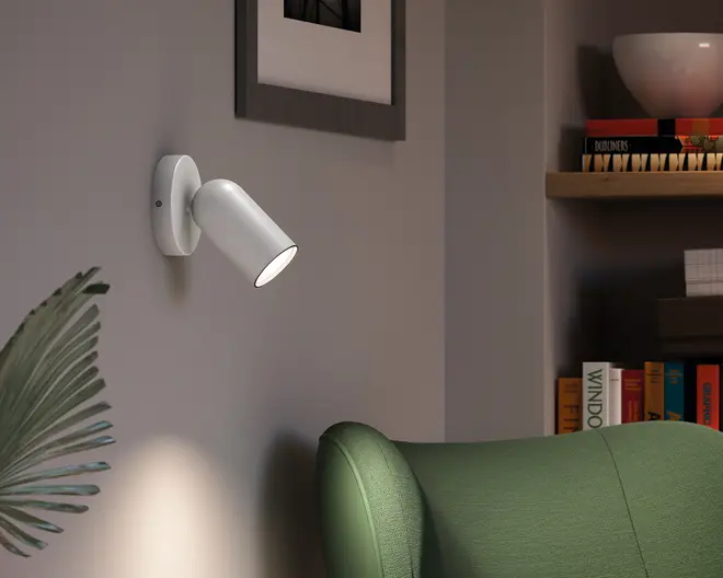 Hvid vægmonteret spotlampe med justerbart cylindrisk lampehoved på en rund bagplade, vinklet nedad og med en fokuseret lysstråle.