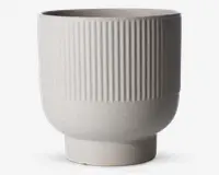 Et moderne, mat hvidligt keramikkar med cylindrisk form. Den øverste halvdel har en lodret rillet tekstur, mens den nederste halvdel er glat og let afrundet, der smalner ind mod bunden. Overfladen har et diskret prikket mønster, som giver et håndlavet udtryk.