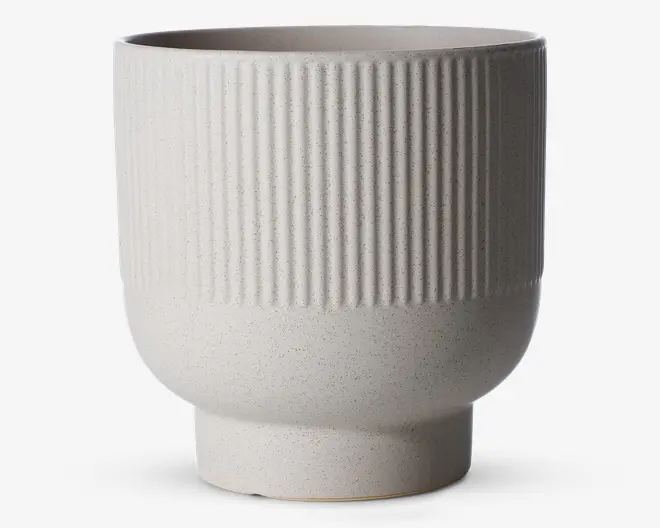 Et moderne, mat hvidligt keramikkar med cylindrisk form. Den øverste halvdel har en lodret rillet tekstur, mens den nederste halvdel er glat og let afrundet, der smalner ind mod bunden. Overfladen har et diskret prikket mønster, som giver et håndlavet udtryk.