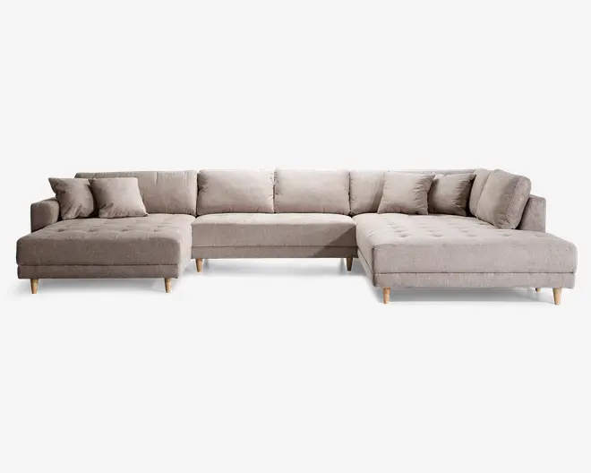 Rummelig L-formet sofa med lyse beige stofbetræk, polstrede sædehynder med knapper og fem løse ryghynder for ekstra komfort. Sofaen har to matchende pyntepuder og står på korte, skrå træben, hvilket giver et moderne og indbydende udtryk. Chaiselong-delen i begge ender giver god plads til afslapning.