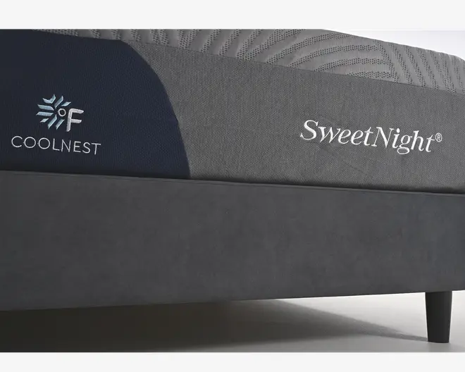 Nærbillede af en madras med tofarvet betræk i mørke- og lysegrå. Sidepanelet har broderet branding, herunder "SweetNight" og "COOLNEST" med et snefnug og temperatursymbol, hvilket indikerer køleteknologi. Stoffet har en tekstureret, mønstret overflade på toppen, hvilket antyder åndbarhed og komfort. Madrassen står på en enkel, mørk sengebund med korte ben.