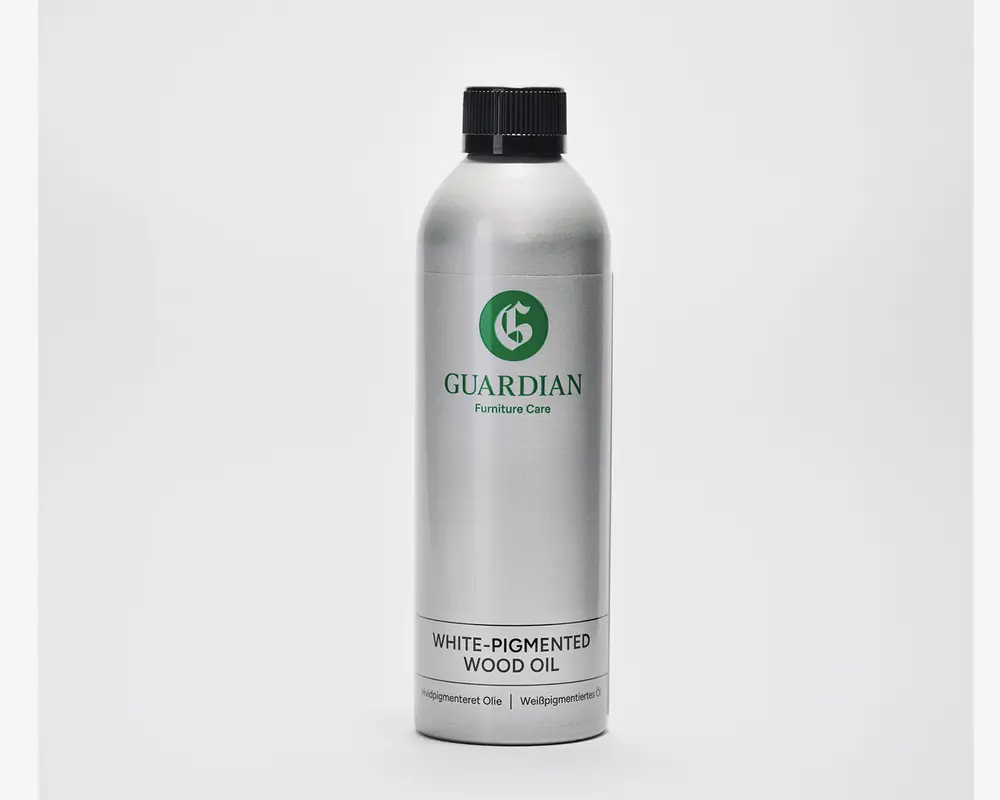 En høj, cylindrisk sølvfarvet metalflaske med sort skruelåg. Etiket med grønt logo og mærket 'Guardian Furniture Care'. Nederst på etiketten står der 'Hvidpigmenteret Olie' med fed sort skrift, og der er yderligere tekst i mindre skrift nedenunder. Designet er enkelt og moderne med et minimalistisk udtryk.