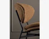 Nærbillede fra siden af en stol med sort metalstel og tyk, tekstureret brun polstring på både sæde og ryglæn. Ryglænet og sædet har et lagdelt, polstret design for ekstra komfort, med afrundede kanter og et moderne, minimalistisk udtryk.
