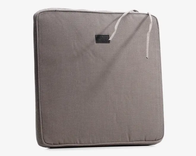 Firkantet pude med et diskret, fintstribet gråt stofbetræk. Har en kant med piping for ekstra holdbarhed og et pænt udseende. To stofsnore i det øverste hjørne gør det muligt at fastgøre puden til en stol. Et lille, rektangulært mærkat er syet fast nær toppen i midten. Puden virker moderat tyk og giver behagelig polstring.