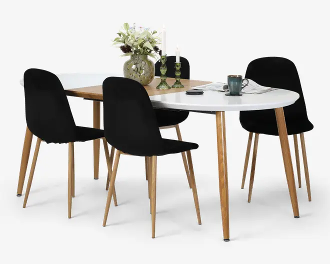 Et moderne spisebordssæt med hvid oval bordplade, en træforlænger, fire sorte polstrede stole med slanke træben samt dekorative ting som en vase med blomster, lysestager og en kop.