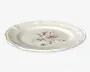 Rund keramiktallerken med let bølget kant og en glat, blank overflade. Midten har et fint blomsterdesign i bløde rosa, lilla og grønne nuancer, hvilket giver tallerkenen et elegant og vintage udtryk.
