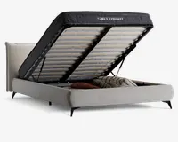 Polstret sengegavl med løftemekanisme, der afslører et rummeligt opbevaringsrum under sengen. Opbevaringsrummet indeholder puder og tæpper, og sengerammen er betrukket med lyse stof og har en polstret hovedgavl samt sorte metalben. Madrassen understøttes af trælameller monteret på en solid metalramme.