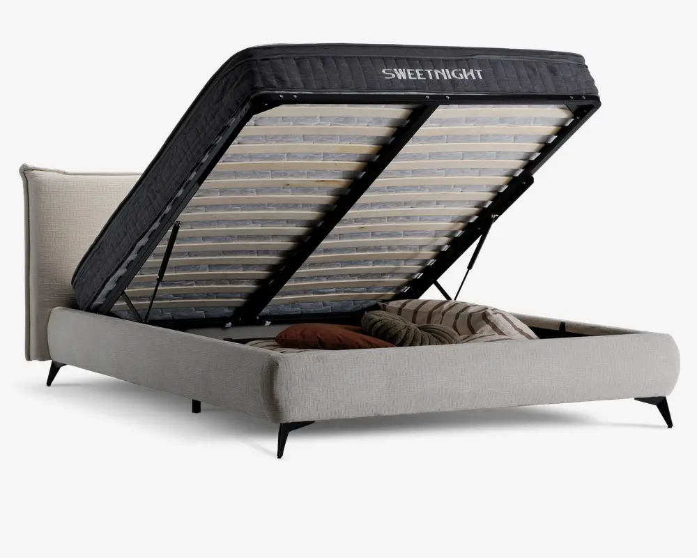 Polstret sengegavl med løftemekanisme, der afslører et rummeligt opbevaringsrum under sengen. Opbevaringsrummet indeholder puder og tæpper, og sengerammen er betrukket med lyse stof og har en polstret hovedgavl samt sorte metalben. Madrassen understøttes af trælameller monteret på en solid metalramme.