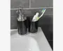 Et sæt matchende badeværelsestilbehør i blank sort med sølvfarvede detaljer. Sættet består af en sæbedispenser med pumpe og et krus, der bruges til at holde en tandbørste og tandpasta. Designet er moderne og stilrent med glatte, cylindriske former og en reflekterende overflade. Produkterne står på en hvid håndvask foran en mørkegrå flisevæg.